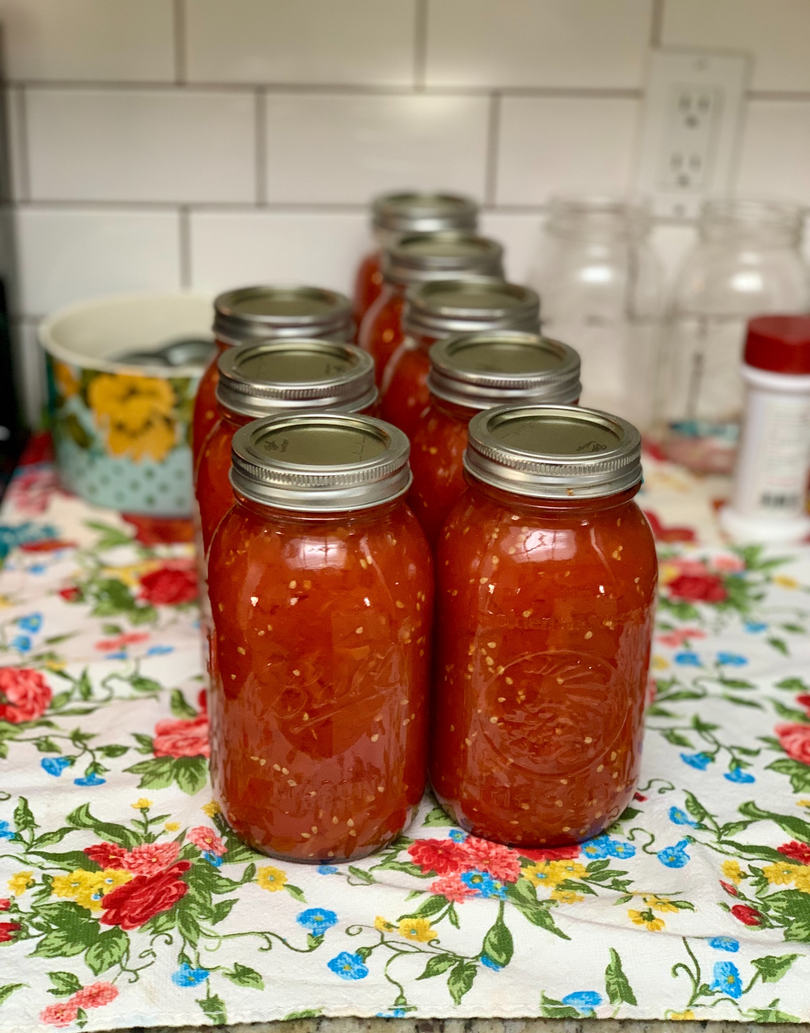 Glass jars filled with tomatoes on a floral cloth in the kitchen